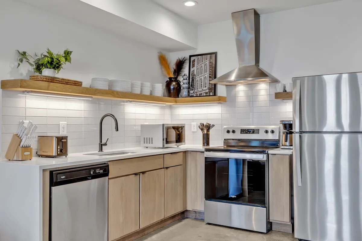 This kitchen scene features gleaming stainless steel appliances, open shelving, a kitchen island, and a decorative vase with lush plants. The space feels bright and welcoming, ideal for cooking or entertaining guests.