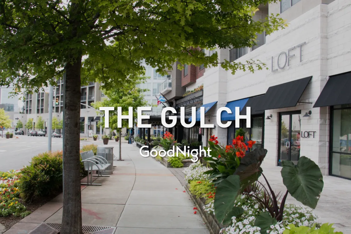 A welcoming, tree-lined sidewalk bordered by flower beds and boutique storefronts, ideal for exploring Nashville’s trendy neighborhoods like 12 South and The Gulch. The scene invites leisurely strolls, shopping, and socializing.