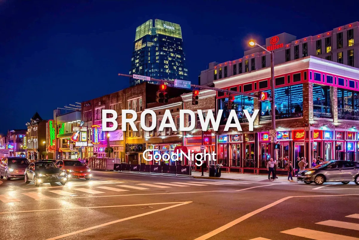 A dynamic street view of Broadway at night, buzzing with people, illuminated neon signs, and high-rise buildings. The scene is alive with energy, capturing Nashville’s iconic nightlife and entertainment district.