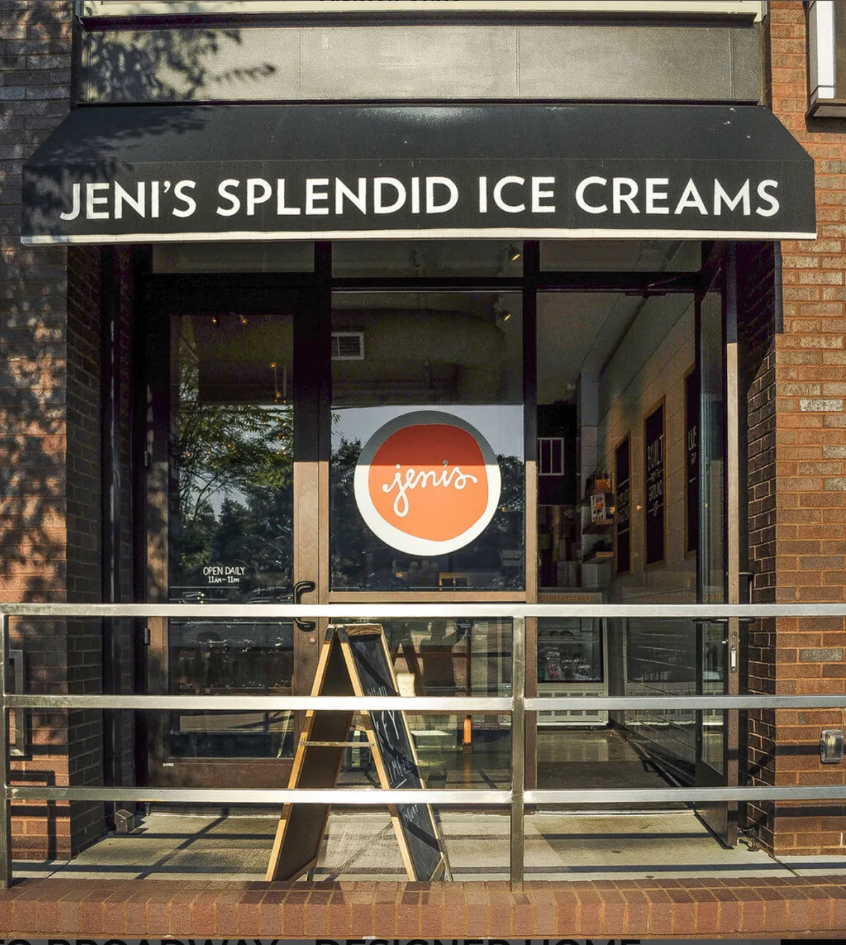 This exterior image captures the cheerful storefront and inviting outdoor seating area of Jeni's Splendid Ice Creams, featuring bright signage and a menu board. Groups of friends relax outside, enjoying ice cream and soaking up the lively neighborhood ambiance.