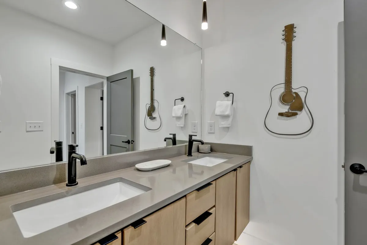 A contemporary bathroom featuring a double sink with a modern faucet, a guitar decoration on the wall, and a clean, creative aesthetic. The dual vanity setup is clearly visible, highlighting the space's spa-inspired functionality.