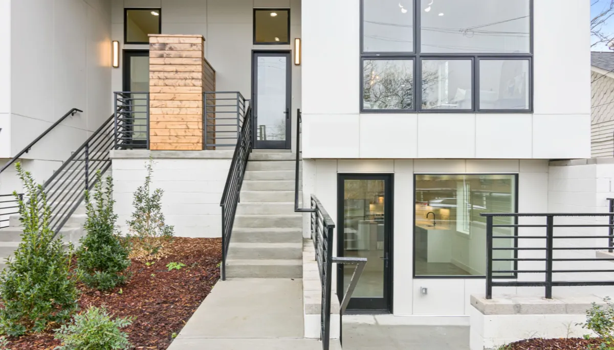 This image showcases the exterior entrance of the property, featuring a contemporary wooden structure, large windows, attractive landscaping, and a welcoming staircase. The area feels open and inviting, setting the stage for guests and their pets stepping out to explore the city.