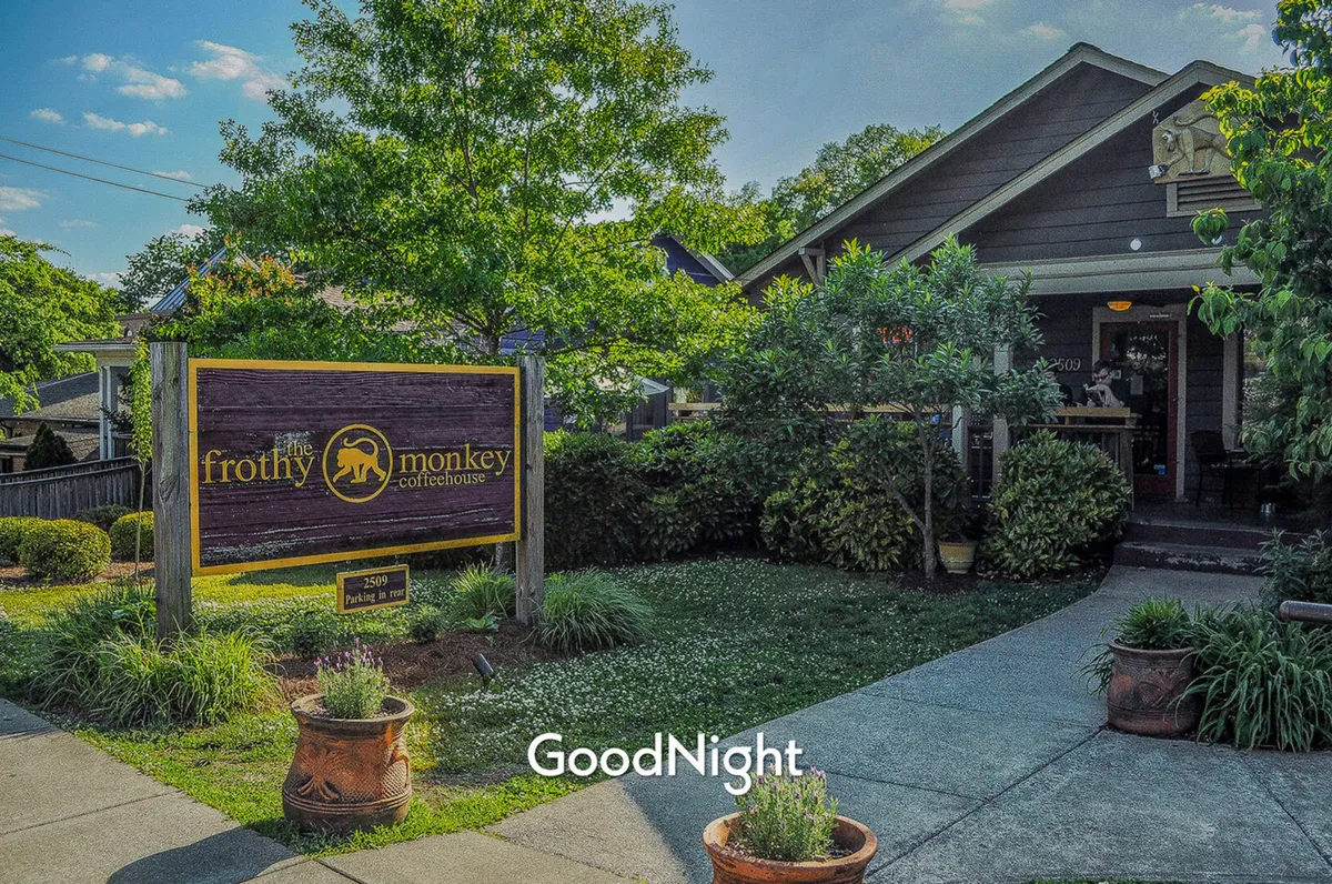 This image features the iconic sign and entrance of Frothy Monkey coffeehouse, surrounded by lush greenery. The inviting storefront and outdoor seating hint at a relaxed atmosphere, perfect for enjoying coffee or a light breakfast.