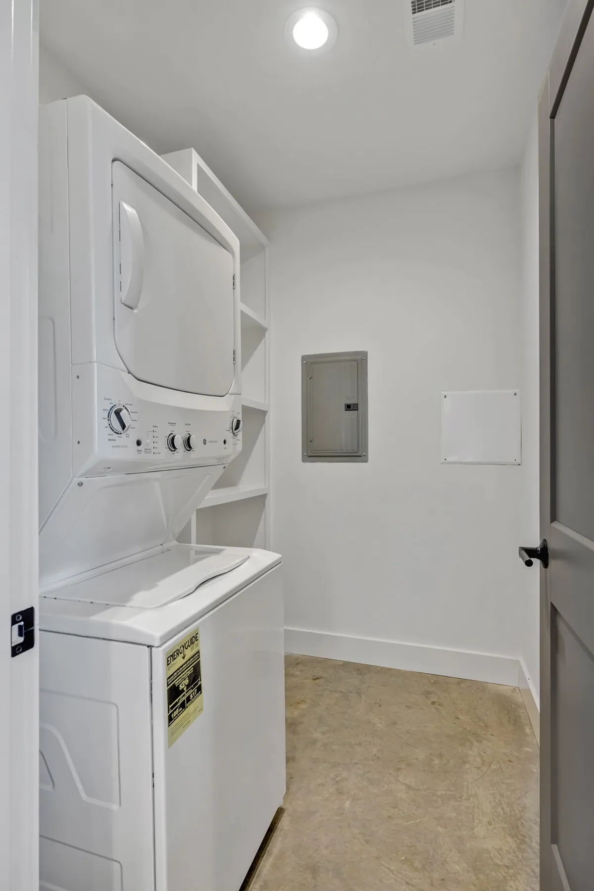 A practical laundry area showing a stacked washer and dryer with storage shelves and an electrical panel. The space is organized and efficient, making it easy for guests on longer stays or families to manage daily chores with ease.
